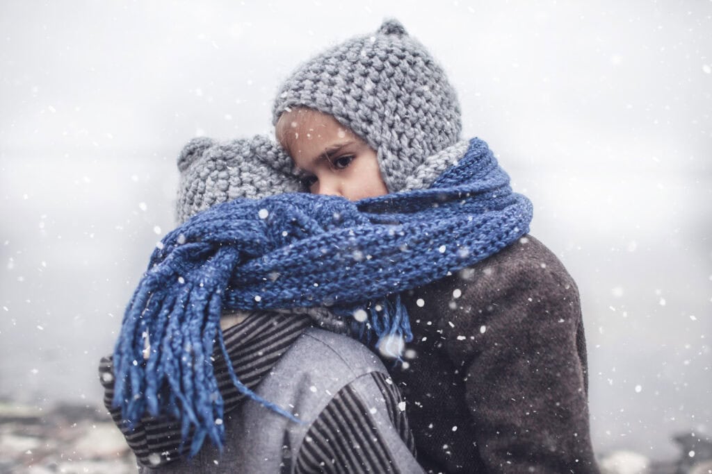 girl in knitted grey hat hugging her frozen smaller brother